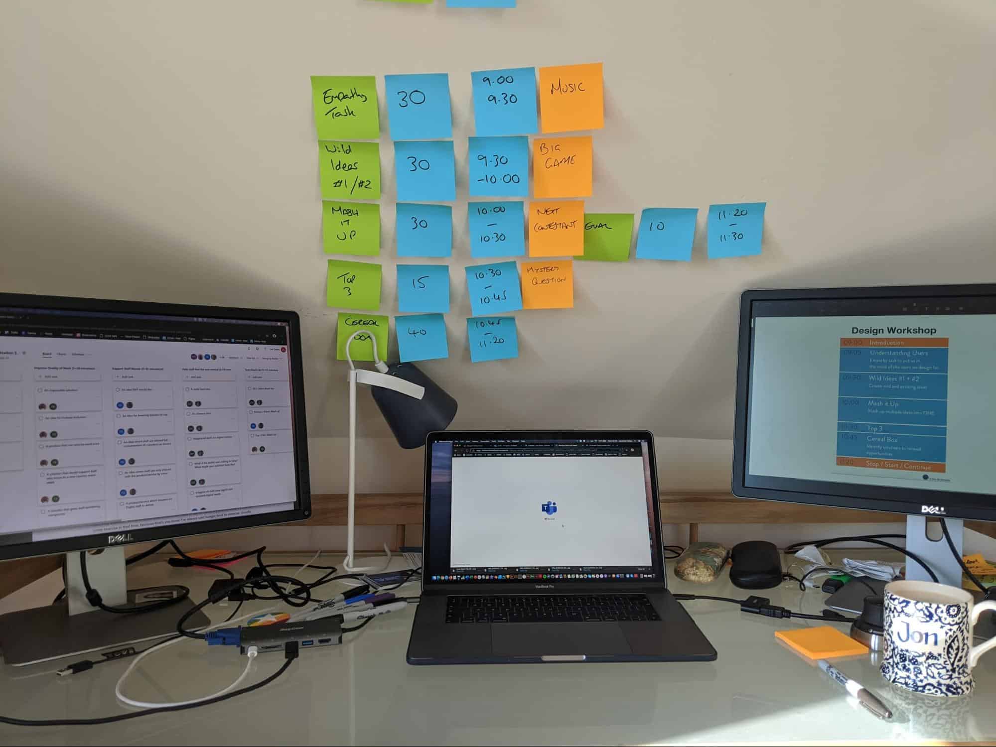 Three computers on a desk with post-it notes on the wall